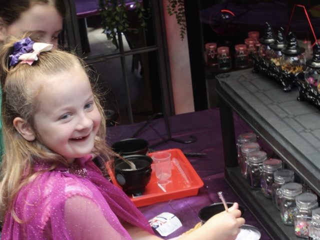 A girl in a pink fairy cloak at the potion table