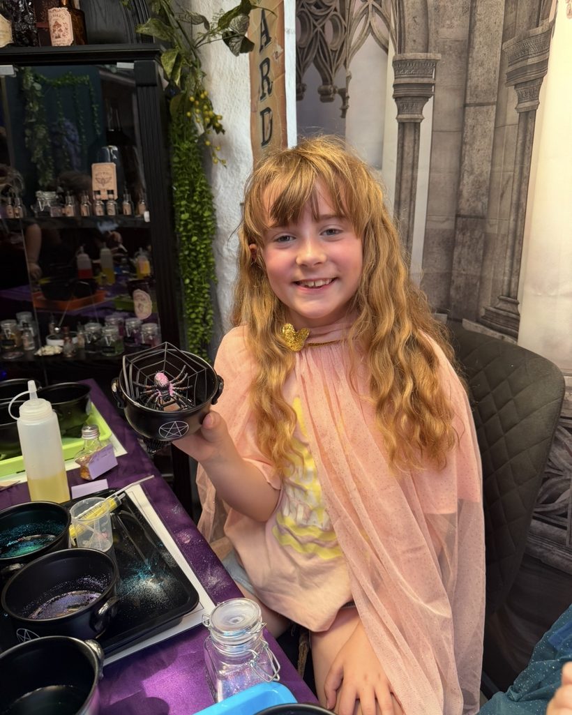A girl in a pink fairy cloak holding her finished potion and a spider-web bowl