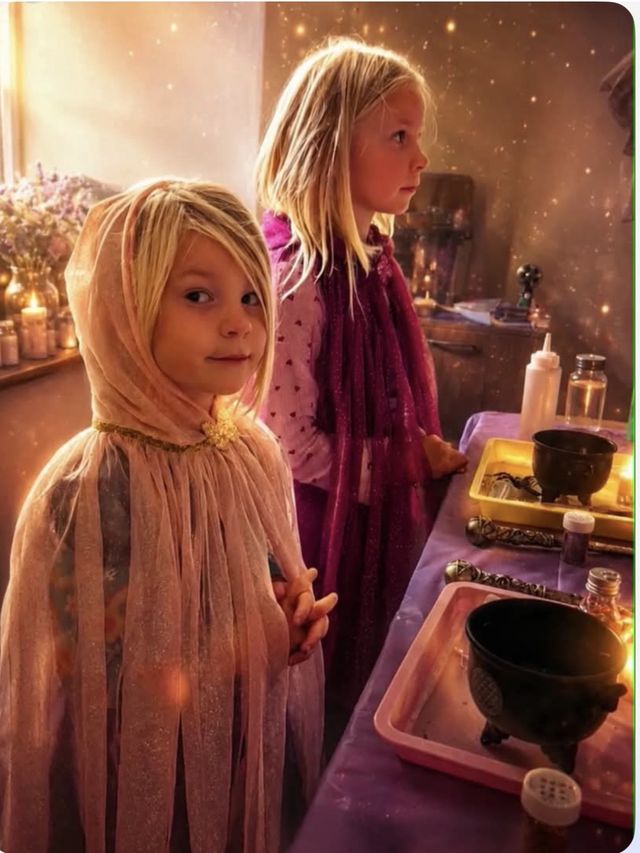 Two girls in fairy capes beside candlelit cauldrons