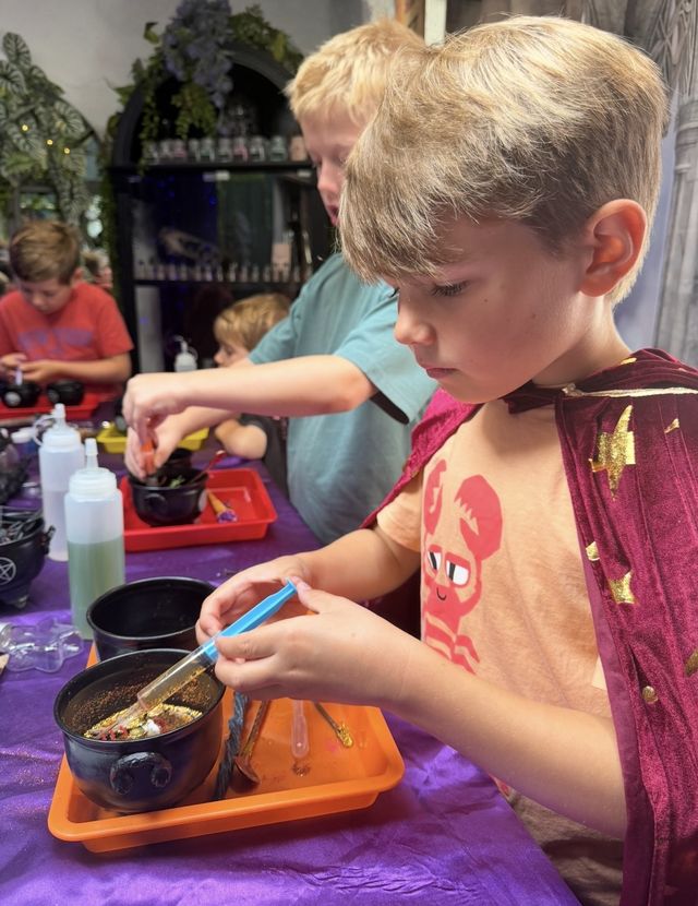 A boy in a cape spooning ingredients into his cauldron