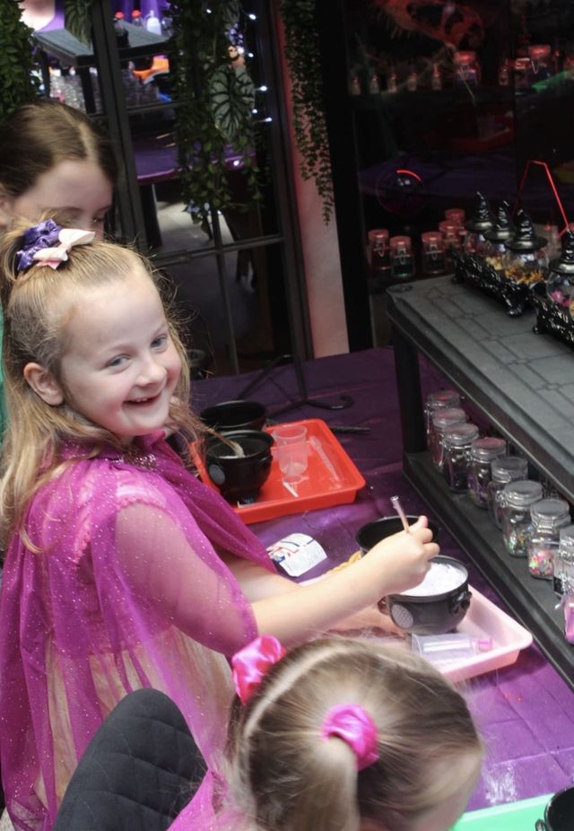 A girl in a pink fairy cape smiling at the bench
