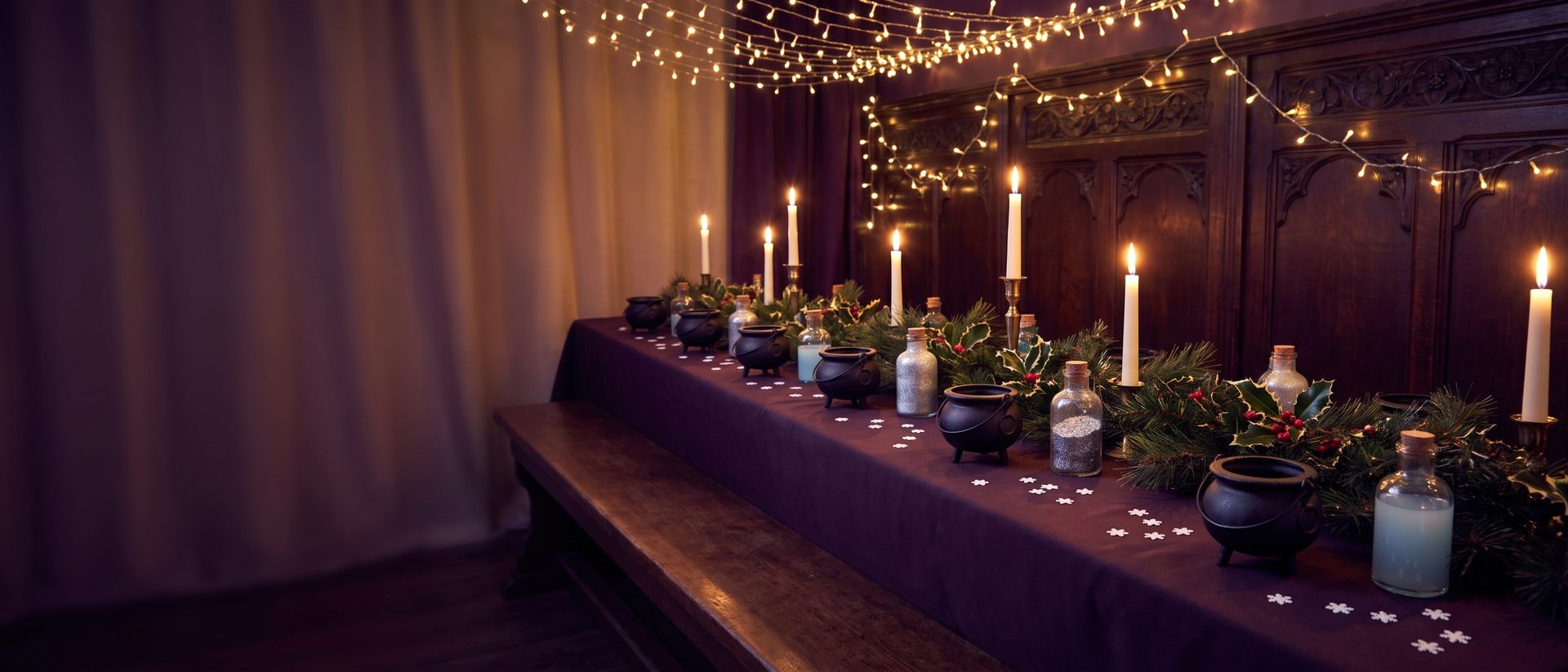 Cauldrons and glitter-filled potion bottles on a purple cloth with pine, holly, candles and fairy lights
