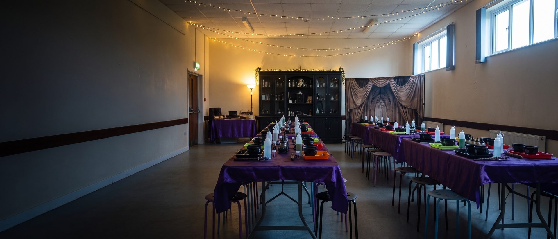 A village hall laid out with tables and cauldrons before a party
