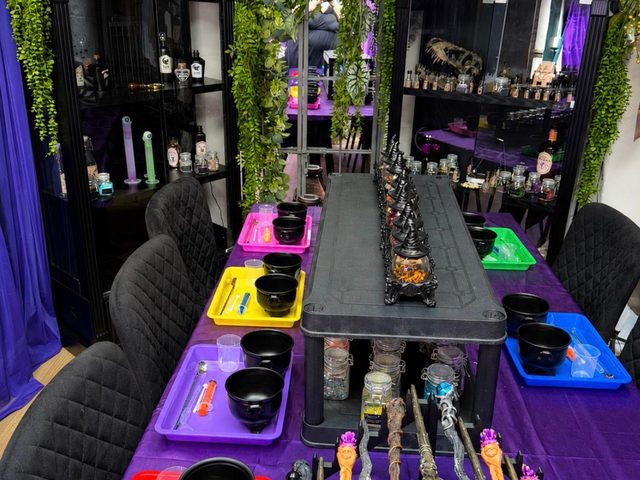 The Potion Room laid out for a party: cauldrons and wands on a purple cloth under lit cabinets of potion bottles