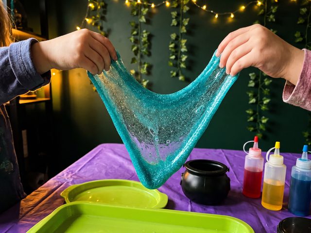 Two pairs of children's hands stretching a wide sheet of turquoise glitter slime
