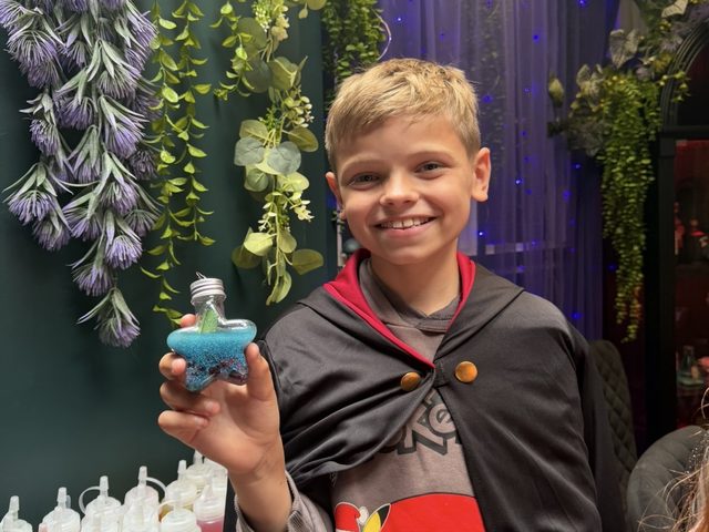 A boy in a wizard cloak holding up the star-shaped potion bottle he made