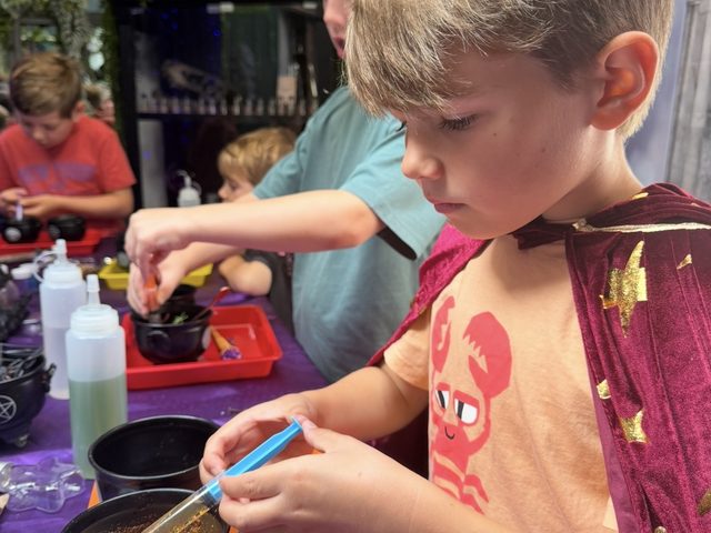 A boy concentrating hard as he stirs a cauldron with a pipette