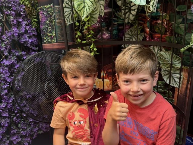 Two boys in wizard cloaks giving a thumbs up
