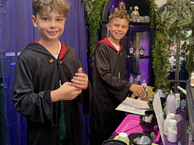 Two boys in black wizard robes at the potion bench